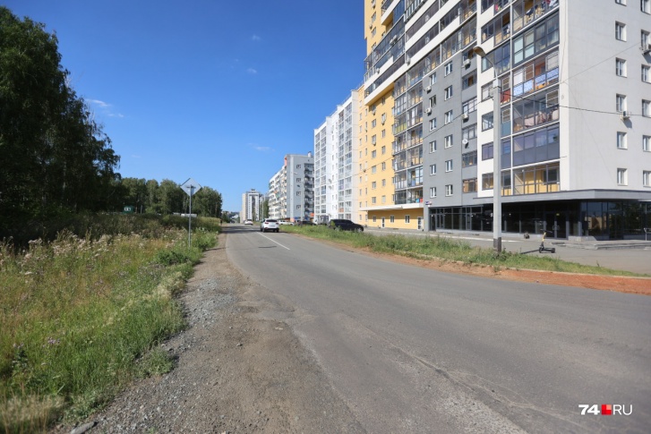 В этом месте сейчас проезжая часть с одной полосой в каждом направлении. С одной стороны дороги — жилые дома, с другой — зеленая зона В этом месте сейчас проезжая часть с одной полосой в каждом направлении. С одной стороны дороги — жилые дома, с другой — зеленая зона