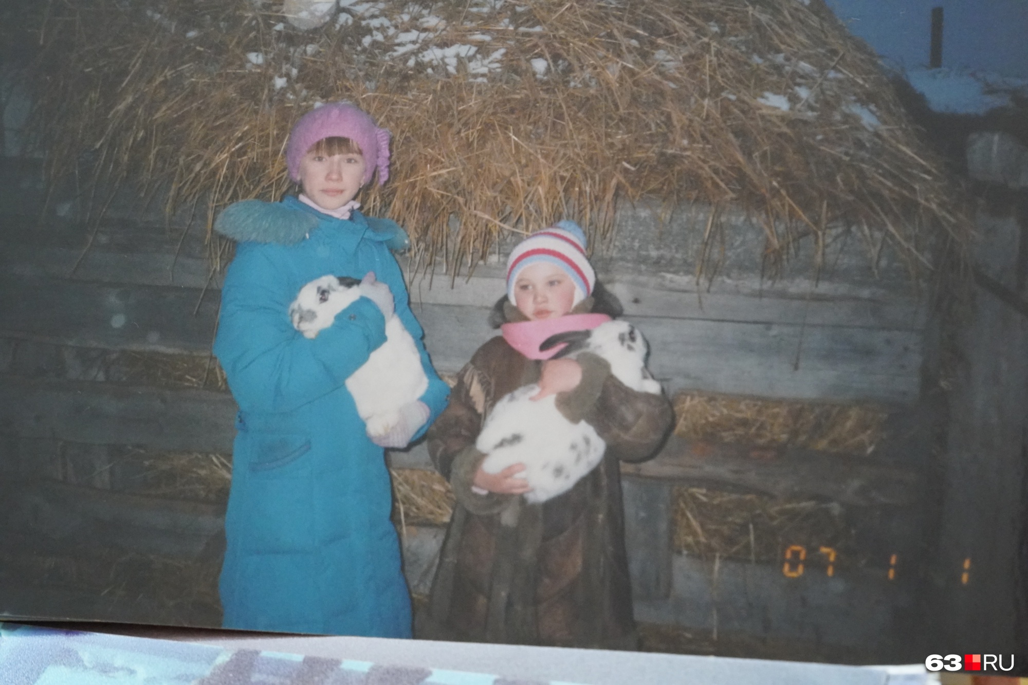 Маленькая Аленка стоит в коричневой шубке. Домашнее хозяйство с кроликами в то время держал ее дедушка
