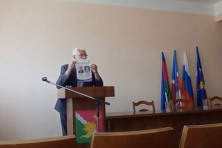 Владимир Дикий держит в руках листовку «Единой России» и объясняет жителям, как принять участие в предварительном голосовании