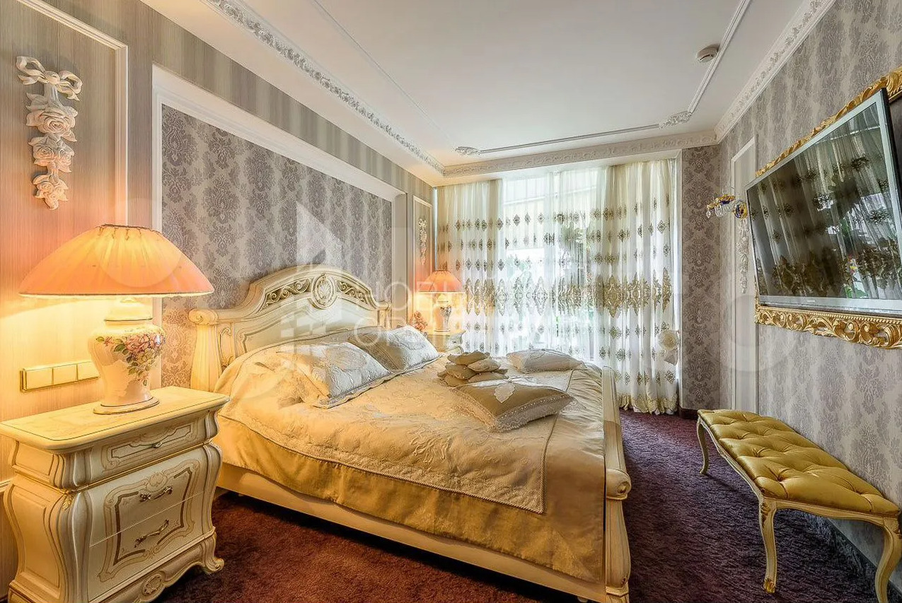 В спальне стоит большая кровать, а напротив — телевизор в массивной золотой раме