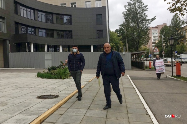 Отец и сын — он же подсудимый — подходят к зданию суда. На заднем плане — одиночный пикет женщины, требующей реального срока для подростка Отец и сын — он же подсудимый — подходят к зданию суда. На заднем плане — одиночный пикет женщины, требующей реального срока для подростка