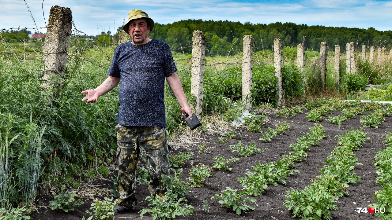 Николай Шермин стоит на краю своего огорода вдоль старой «колючки», ограждающей пойму Течи от людей