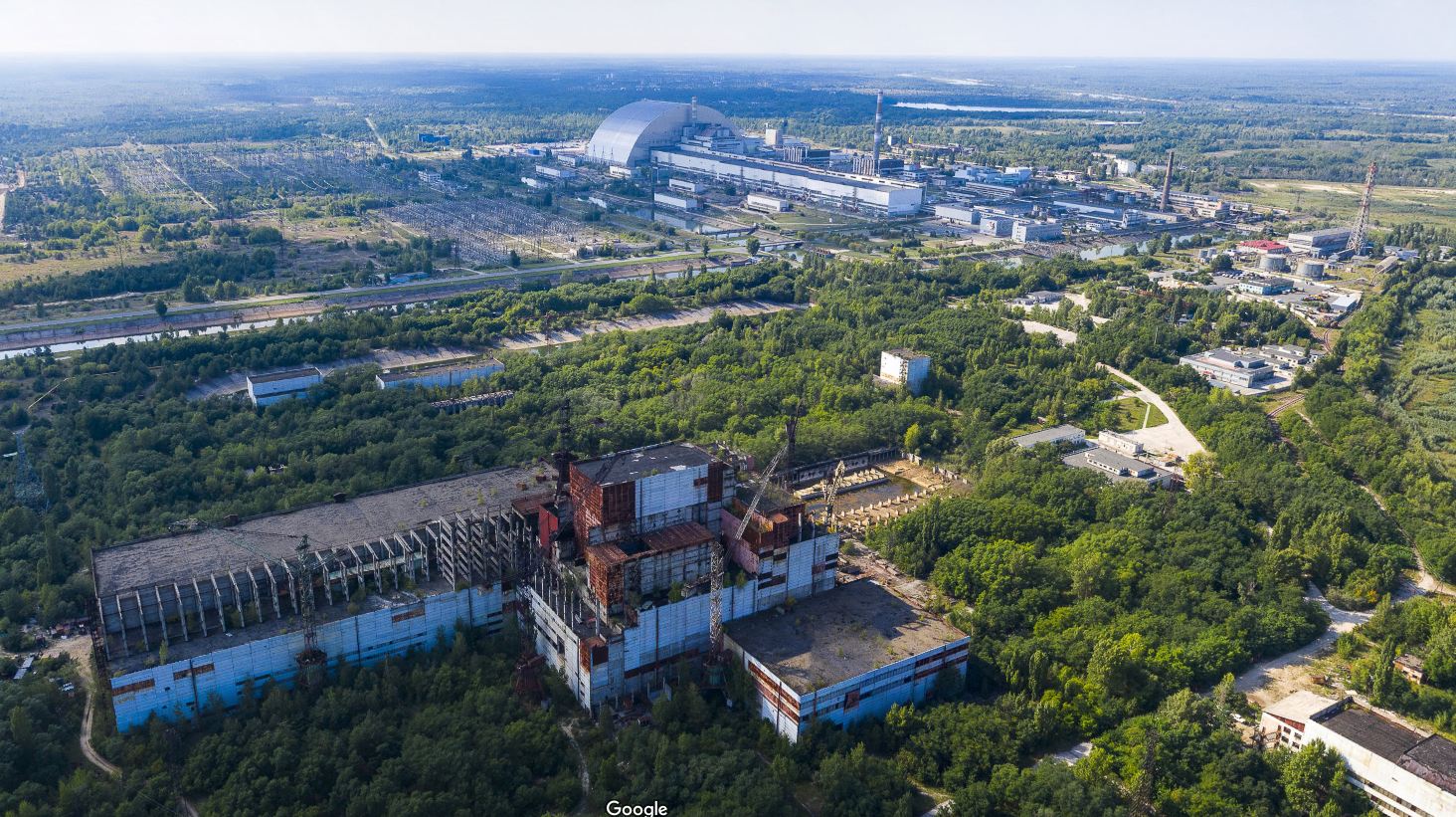 Окрестности Чернобыльской АЭС сегодня: на переднем плане виден машинный зал пятого энергоблока. Первые четыре блока вдалеке, над последним — полукруглый саркофаг