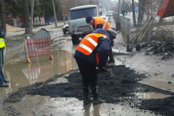 Дорожники засыпают щебенку в яму с лужей Дорожники засыпают щебенку в яму с лужей