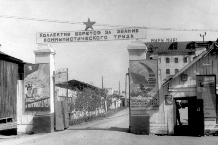 Больше полувека назад за этими воротами располагалась местная сетевязальная фабрика, а дом с надписью «Миру — мир!» когда-то принадлежал купцу Текутьеву, главному меценату дореволюционной Тюмени. Сейчас здесь — рынок «На Минской»<br>