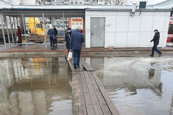 Людям приходится идти к остановке по уложенным в лужу доскам Людям приходится идти к остановке по уложенным в лужу доскам
