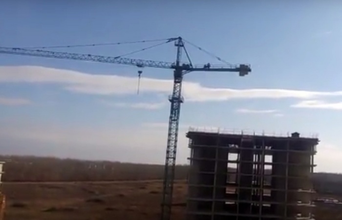 На стреле башенного крана стоят несколько мужчин На стреле башенного крана стоят несколько мужчин