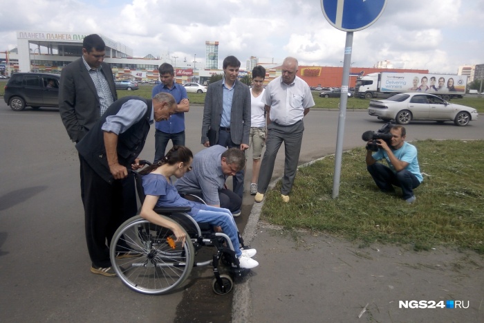 Проехав от остановки по пешеходной дорожке, женщина на коляске остановилась перед высоким бордюром Проехав от остановки по пешеходной дорожке, женщина на коляске остановилась перед высоким бордюром