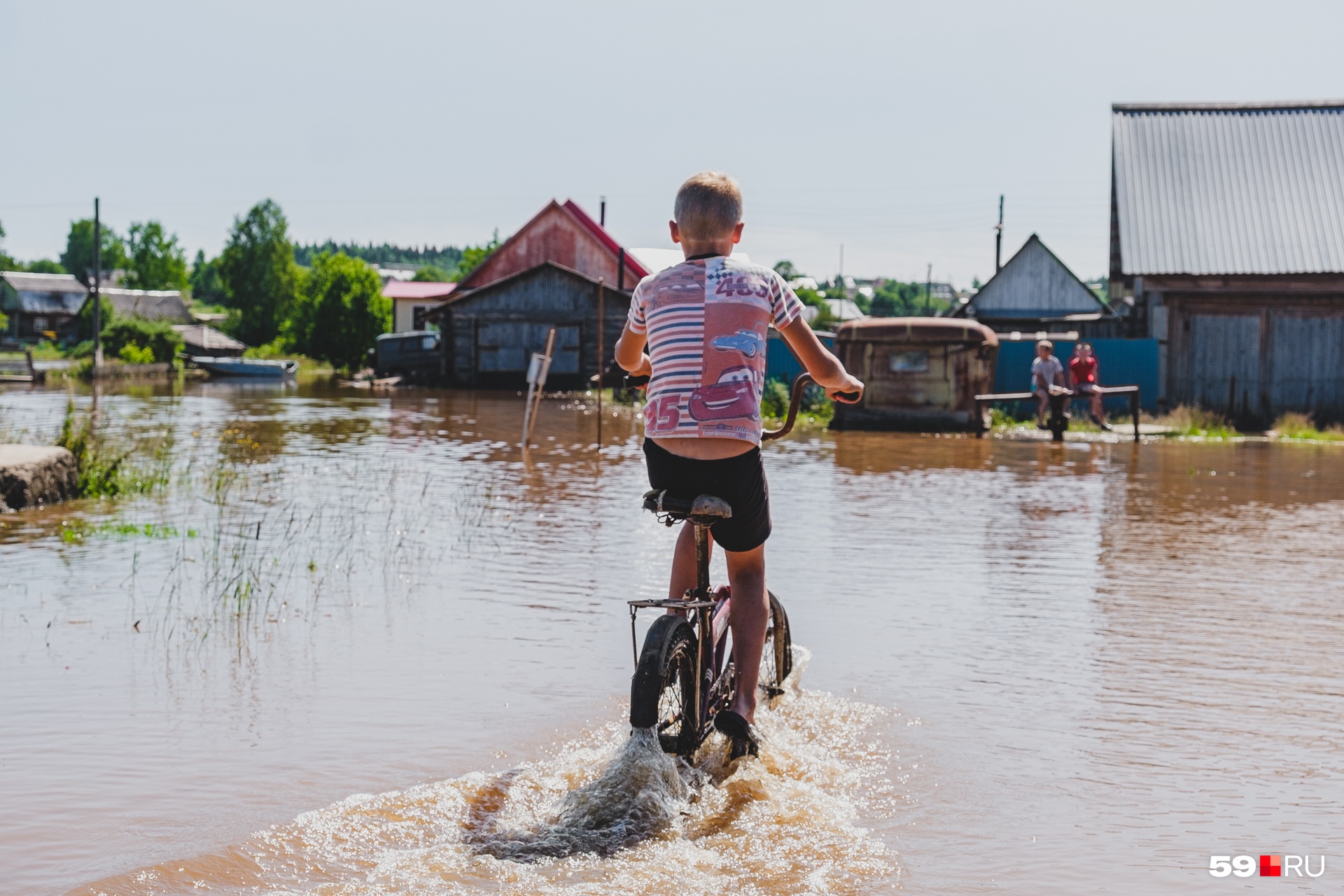 Местный парнишка на велосипеде пересекает затопленную улицу